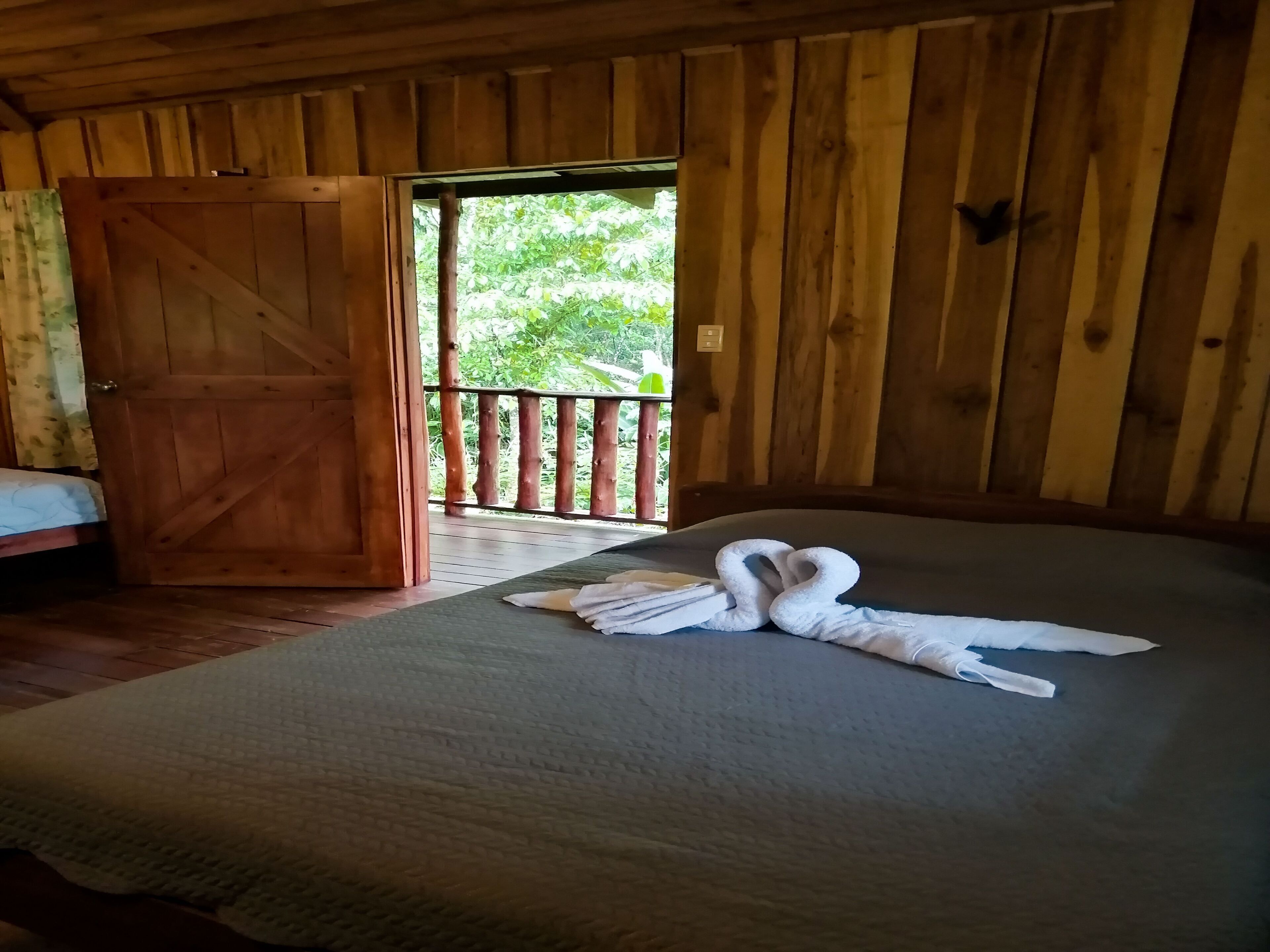Une pièce en bois avec un lit, une porte en bois et un balcon doté d’une balustrade.
