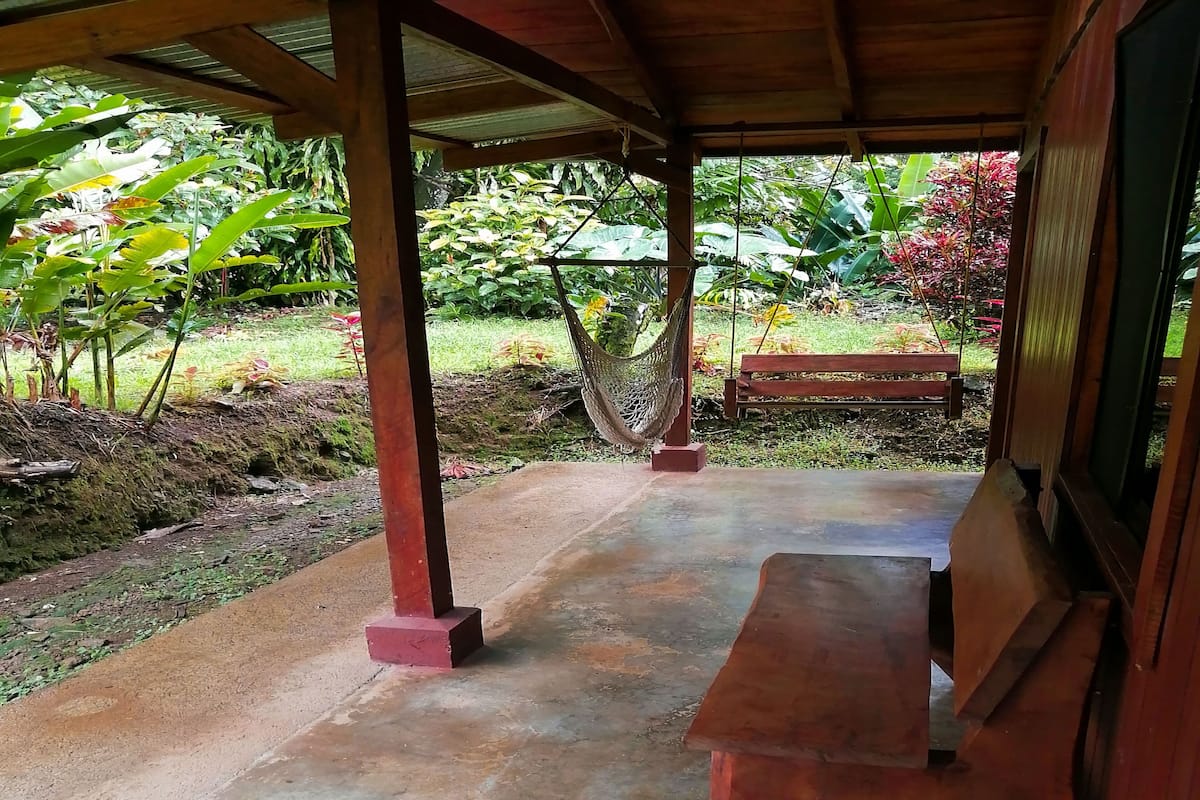 A covered outdoor area with a concrete floor, a hammock, and a wooden bench.