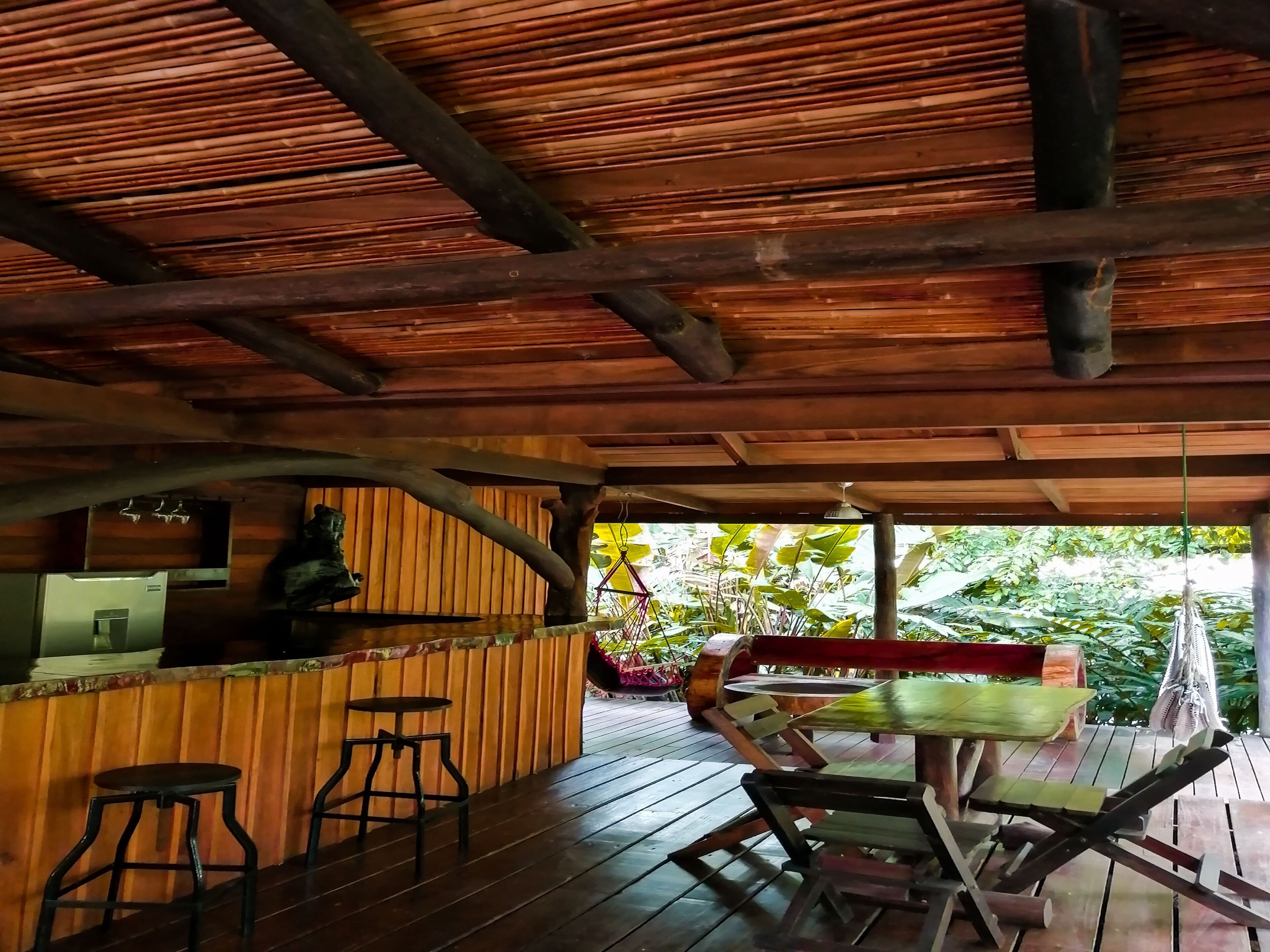 An indoor wooden structure with a bar area, stools, and a table with chairs.