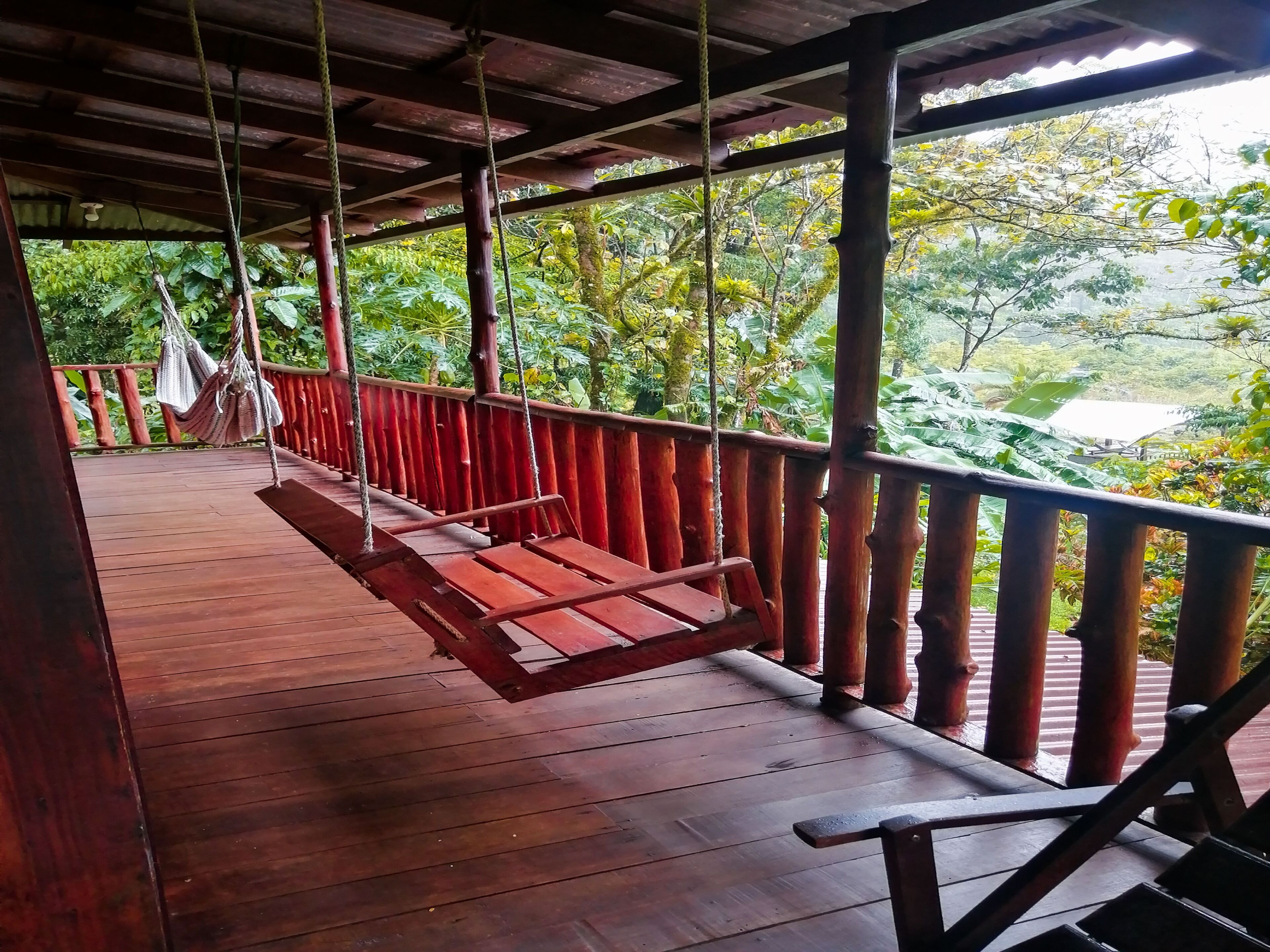 A wooden deck with a swing, surrounded by a wooden railing, overlooking a lush green landscape.