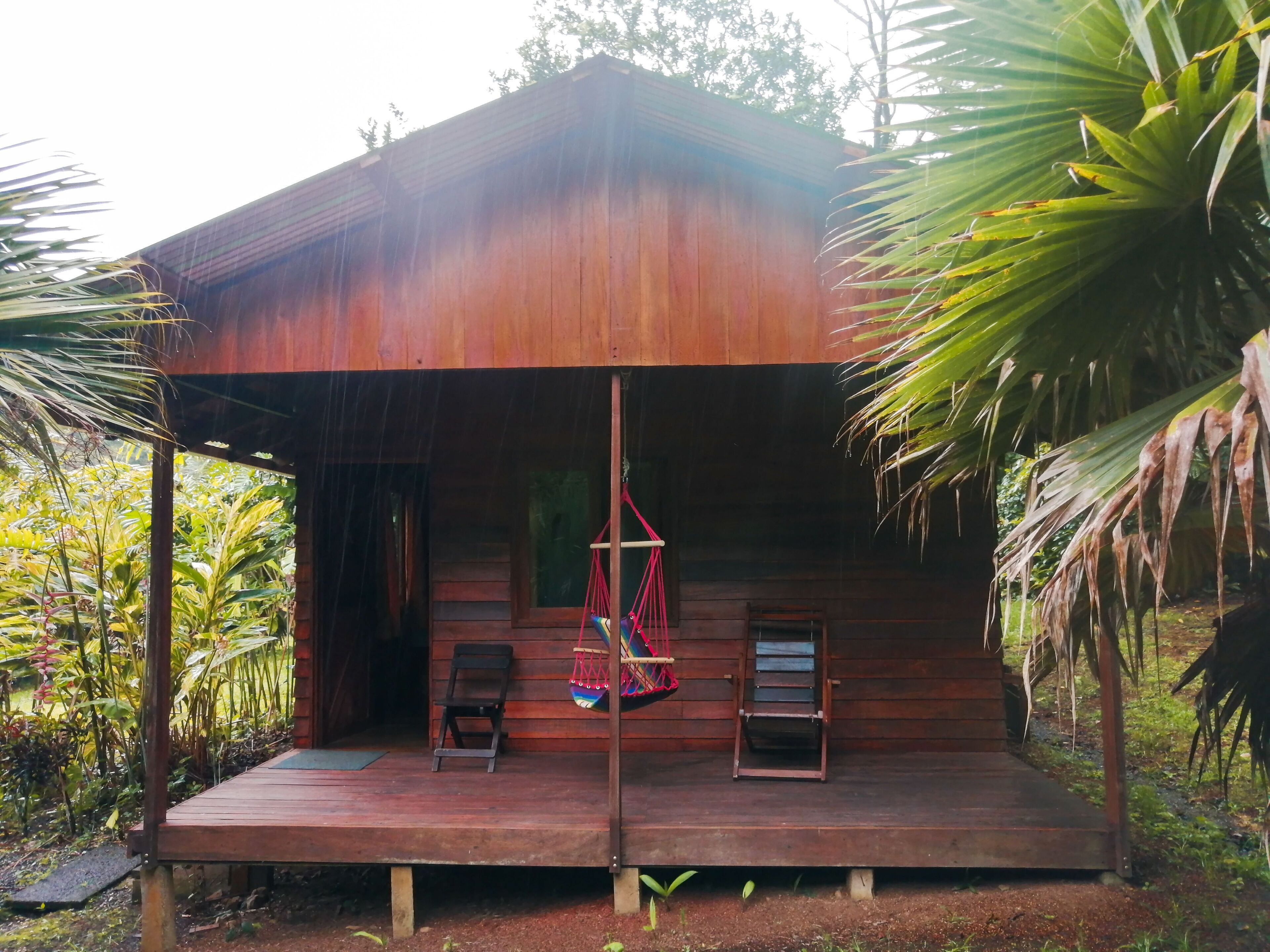 A wooden cabin with a porch, two chairs, and a hammock.
