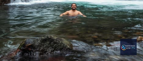 A man in a natural setting with a waterfall and lush greenery.