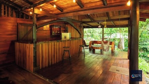 A wooden bar area with stools, a bench, and a hammock. - Cataratas Bijagua Lodge (Bijagua)