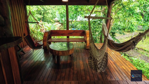 A wooden deck with a hammock, a bench, and a table. - Cataratas Bijagua Lodge (Bijagua)