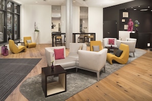 A modern hotel lobby with a seating area, a reception desk, and a dining area.