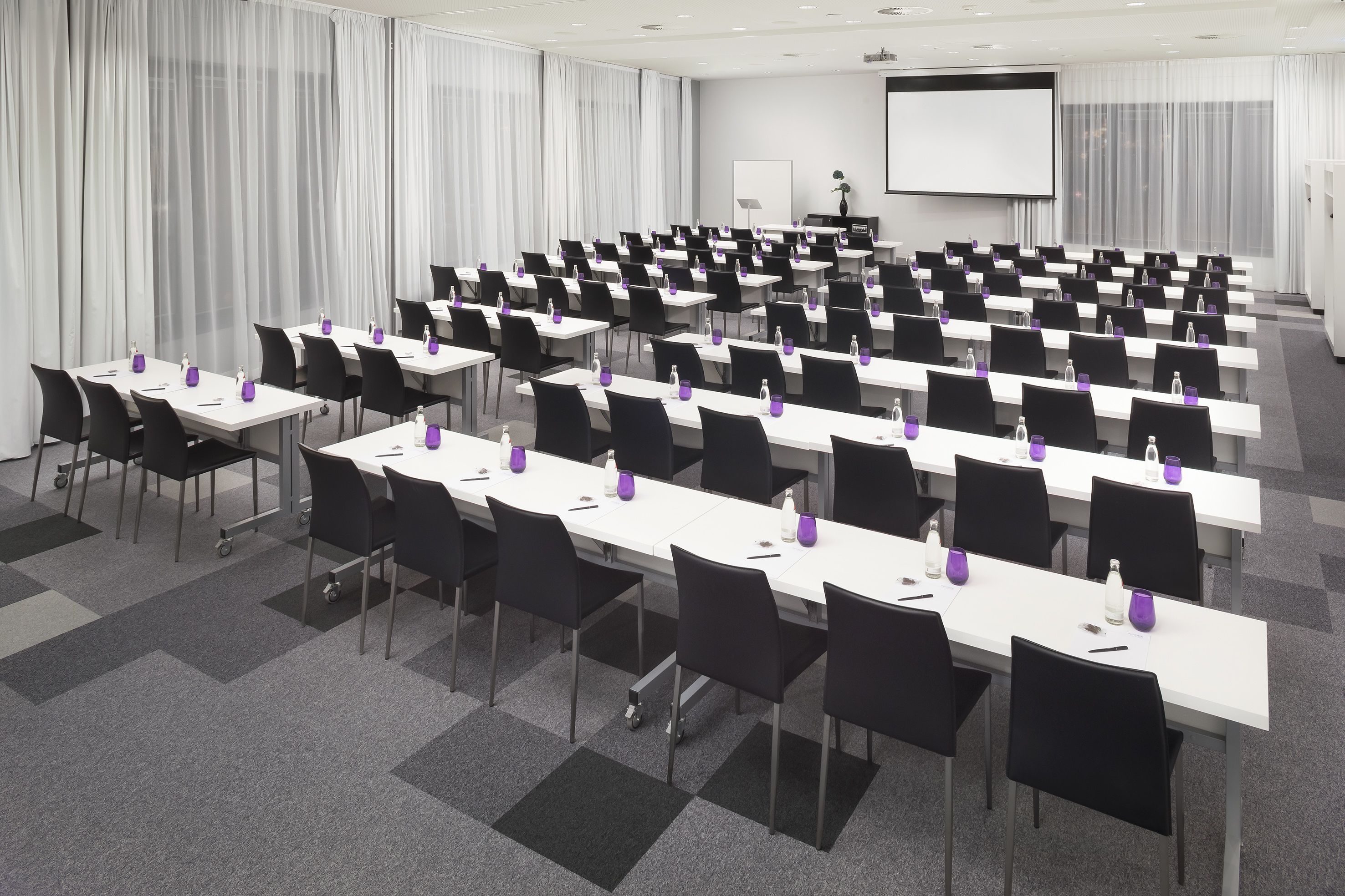 A conference room with rows of tables and chairs, a projector screen, and a whiteboard.