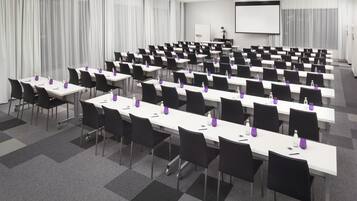A conference room with rows of tables and chairs, a projector screen, and a whiteboard.