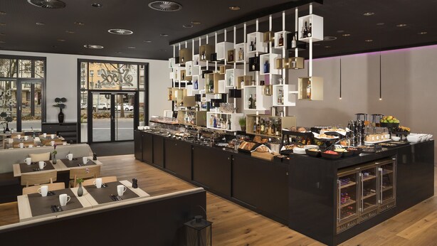 A modern bar area with a variety of beverages and snacks, wooden flooring, and a seating area with tables and chairs. - INNSiDE by Meliá Frankfurt Ostend (Frankfurt)