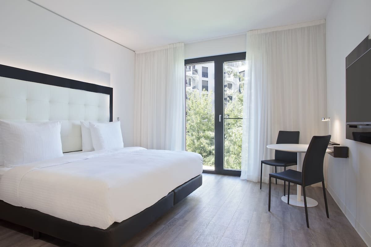 Une chambre d’hôtel moderne avec un grand lit, une table à manger avec des chaises et un balcon avec des rideaux.