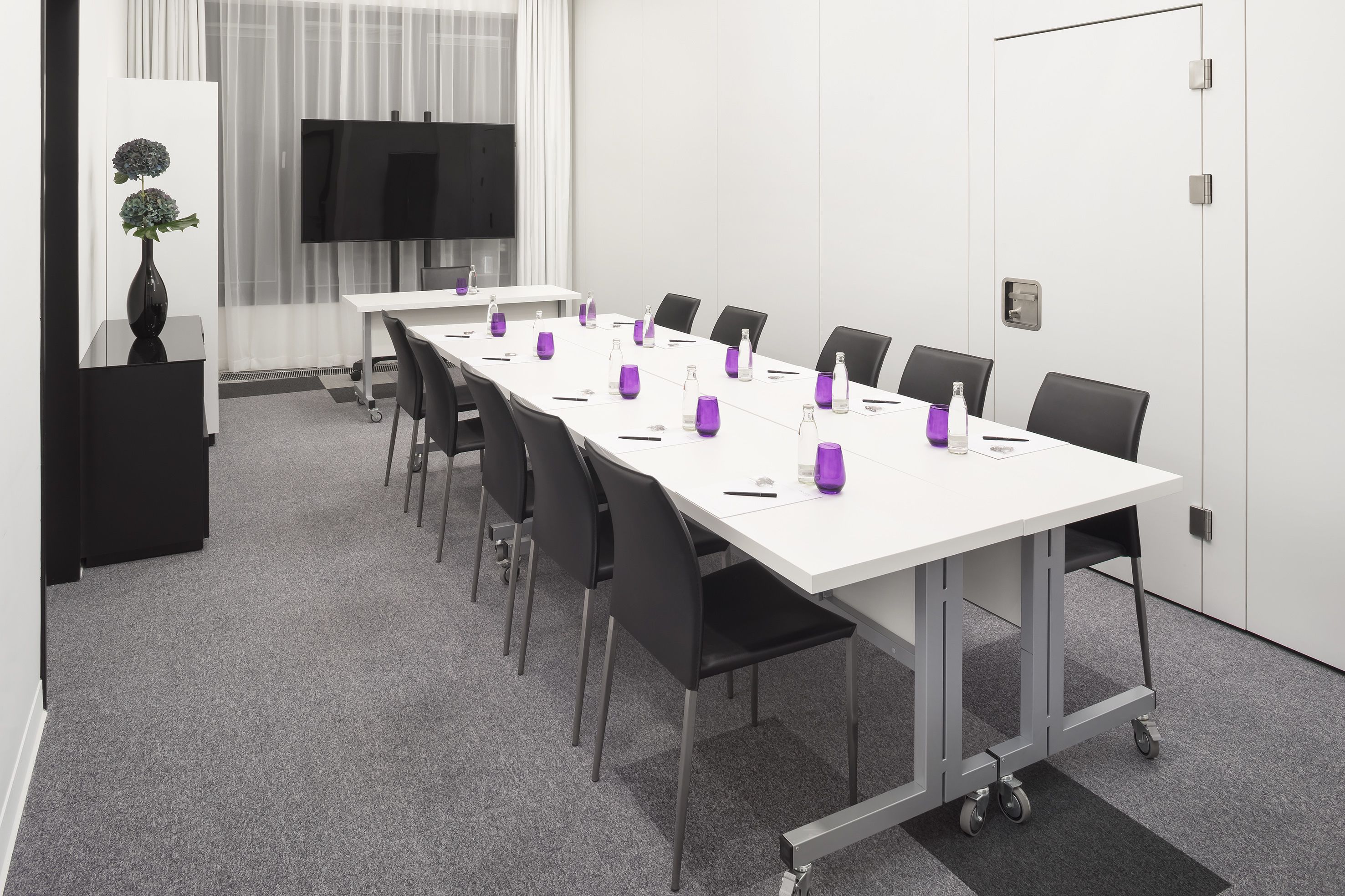 Ein Konferenzraum mit langem Tisch, Stühlen, einem Fernseher und einer Pflanze.