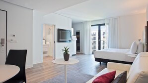 A modern hotel room with a bed, a TV, a small table with a plant, a sofa, and a dining area with chairs. - INNSiDE by Meliá Frankfurt Ostend (Frankfurt)