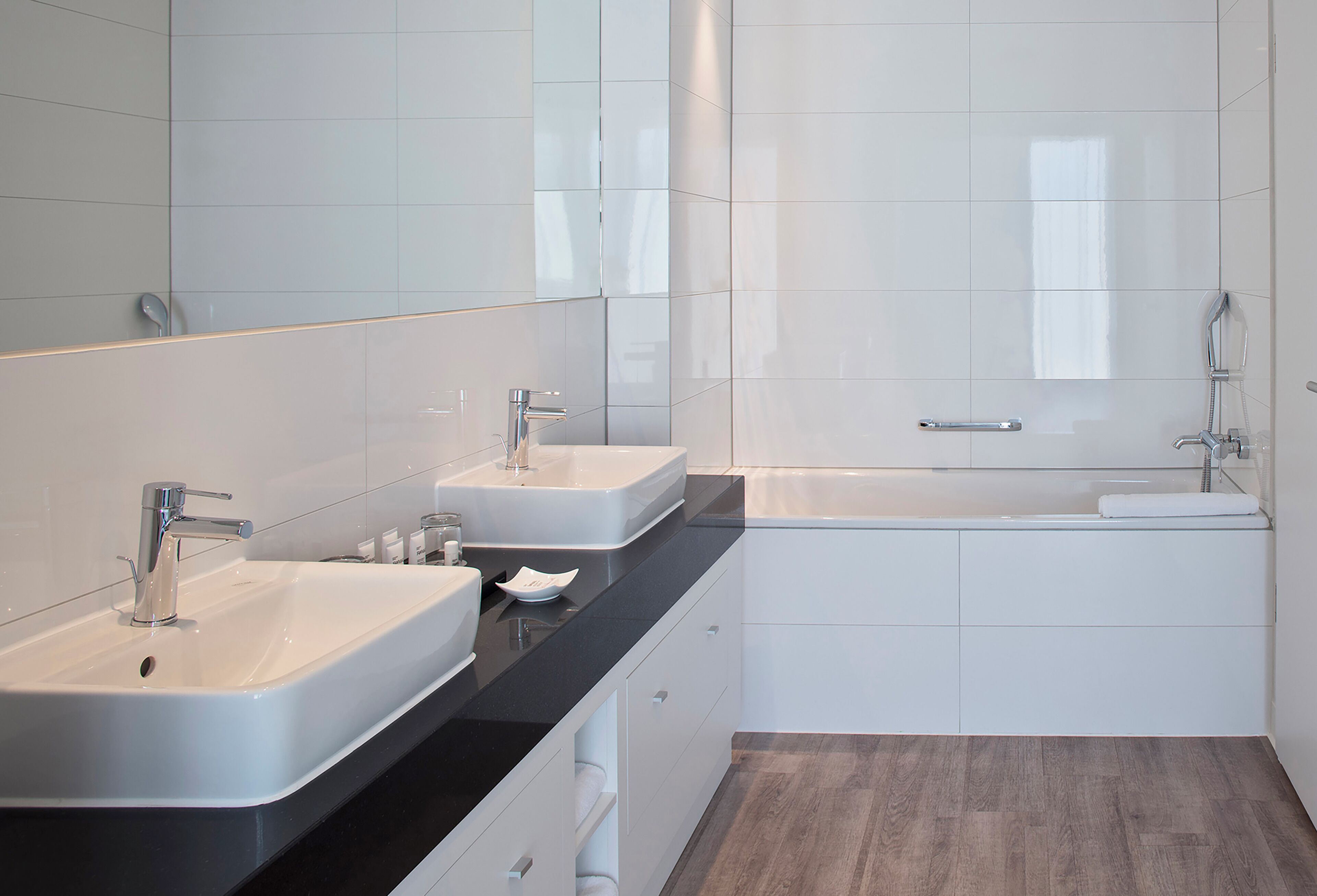 A modern bathroom with two sinks, a bathtub, and a large mirror.