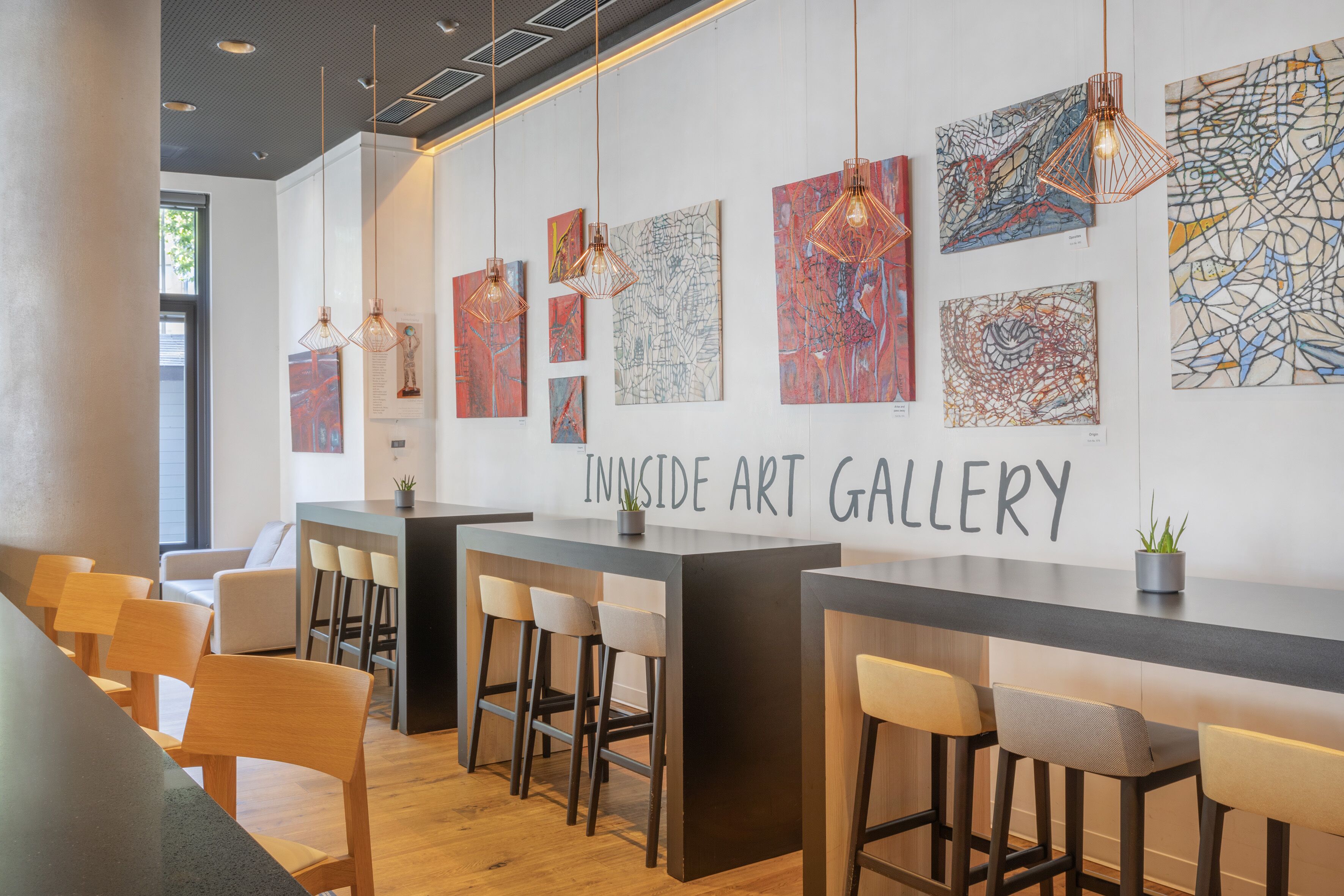 An art gallery with abstract paintings, a bar area, and seating.