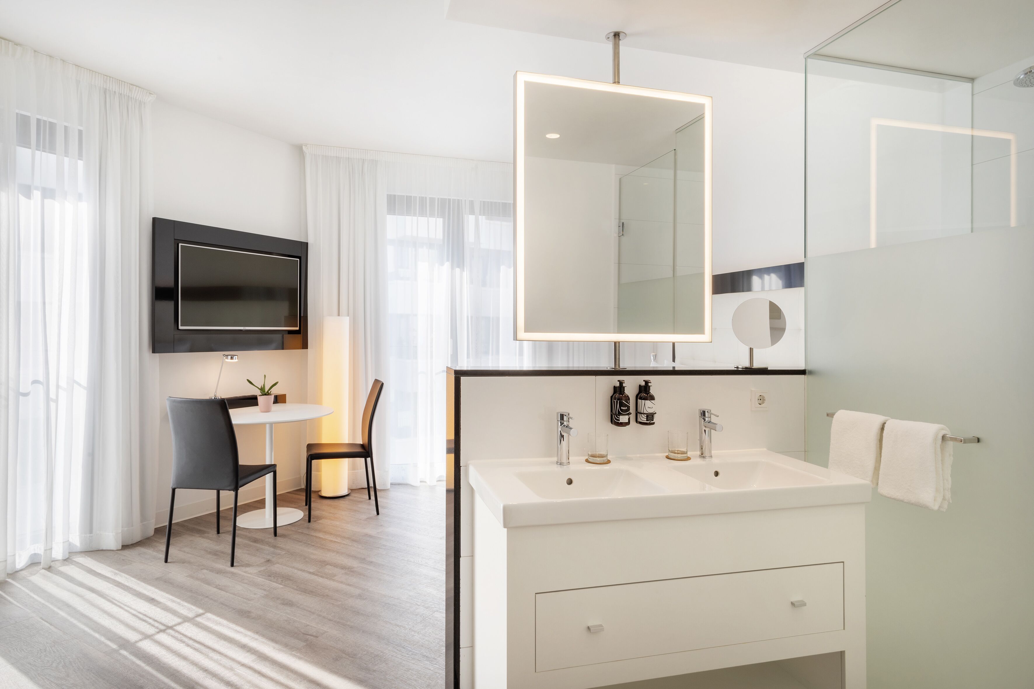 A modern bathroom with a large mirror, two sinks, and a flat-screen TV mounted above the vanity.