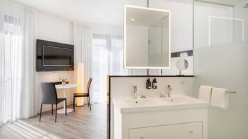 A modern bathroom with a large mirror, two sinks, and a flat-screen TV mounted above the vanity.