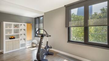 A spacious room with a large window, a treadmill, a white storage unit, and a yoga ball.