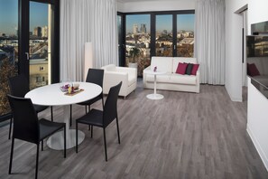 A modern living room with a dining area, large windows, and a city view.