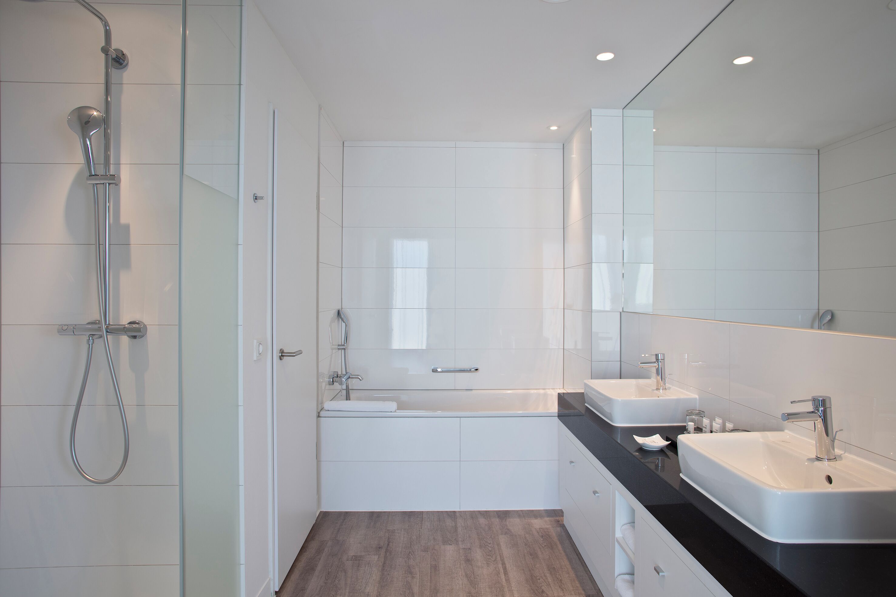 A modern bathroom with a glass shower enclosure, a bathtub, two sinks, and a large mirror.