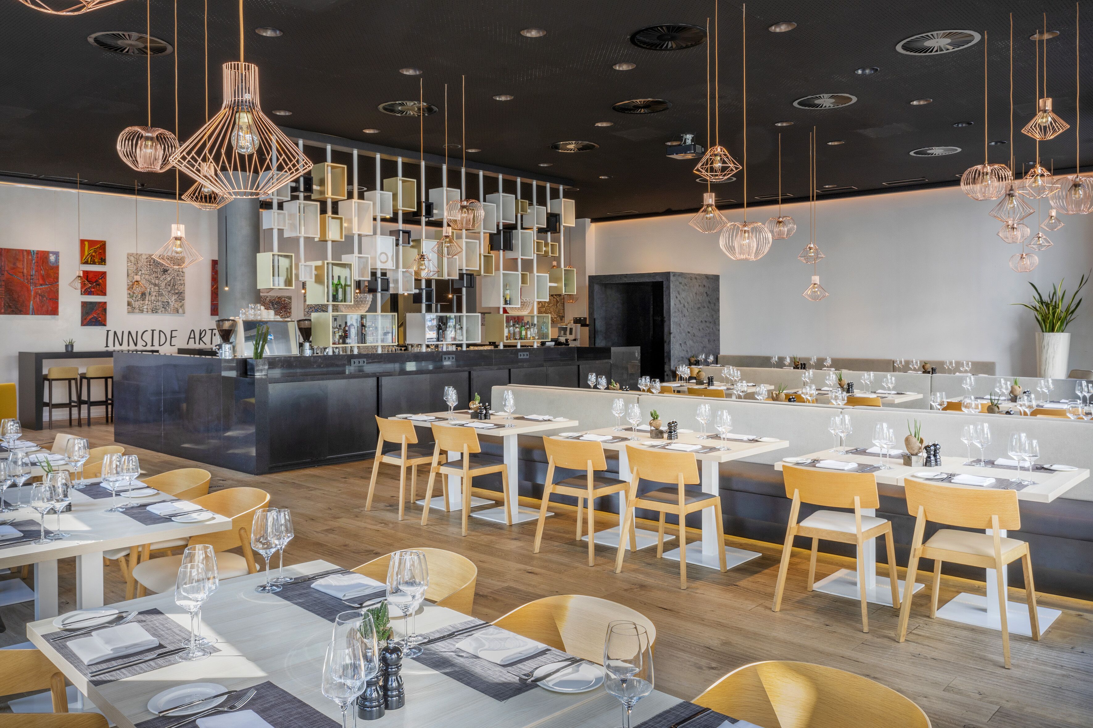 A modern restaurant with a bar area, wooden chairs, and hanging pendant lights.