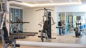 Un gimnasio con diversas máquinas de ejercicio, una cinta de correr y un espejo grande.