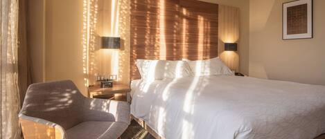 Una habitación de hotel con una cama, una silla, una mesita de noche y lámparas fijadas a la pared.