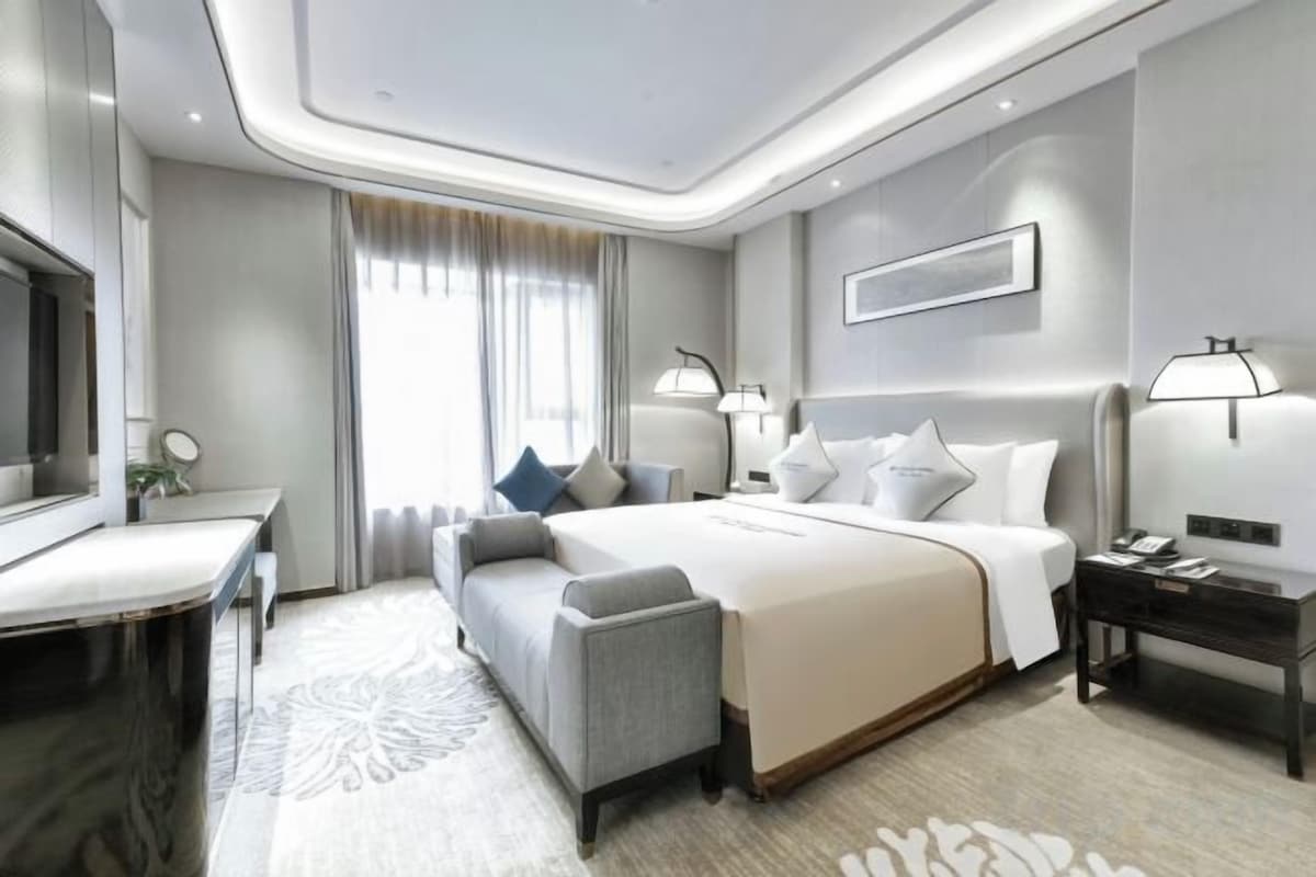 A modern hotel room with a large bed, bedside tables, a desk, and a television.