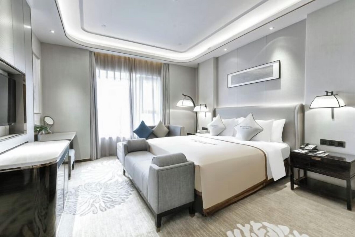 A modern hotel room with a large bed, a desk, a sofa, and a TV.