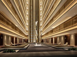 Eine moderne Hotellobby mit einer zentralen Skulptur, verschiedenen Sitzbereichen und einer hohen Decke mit linearer Beleuchtung.