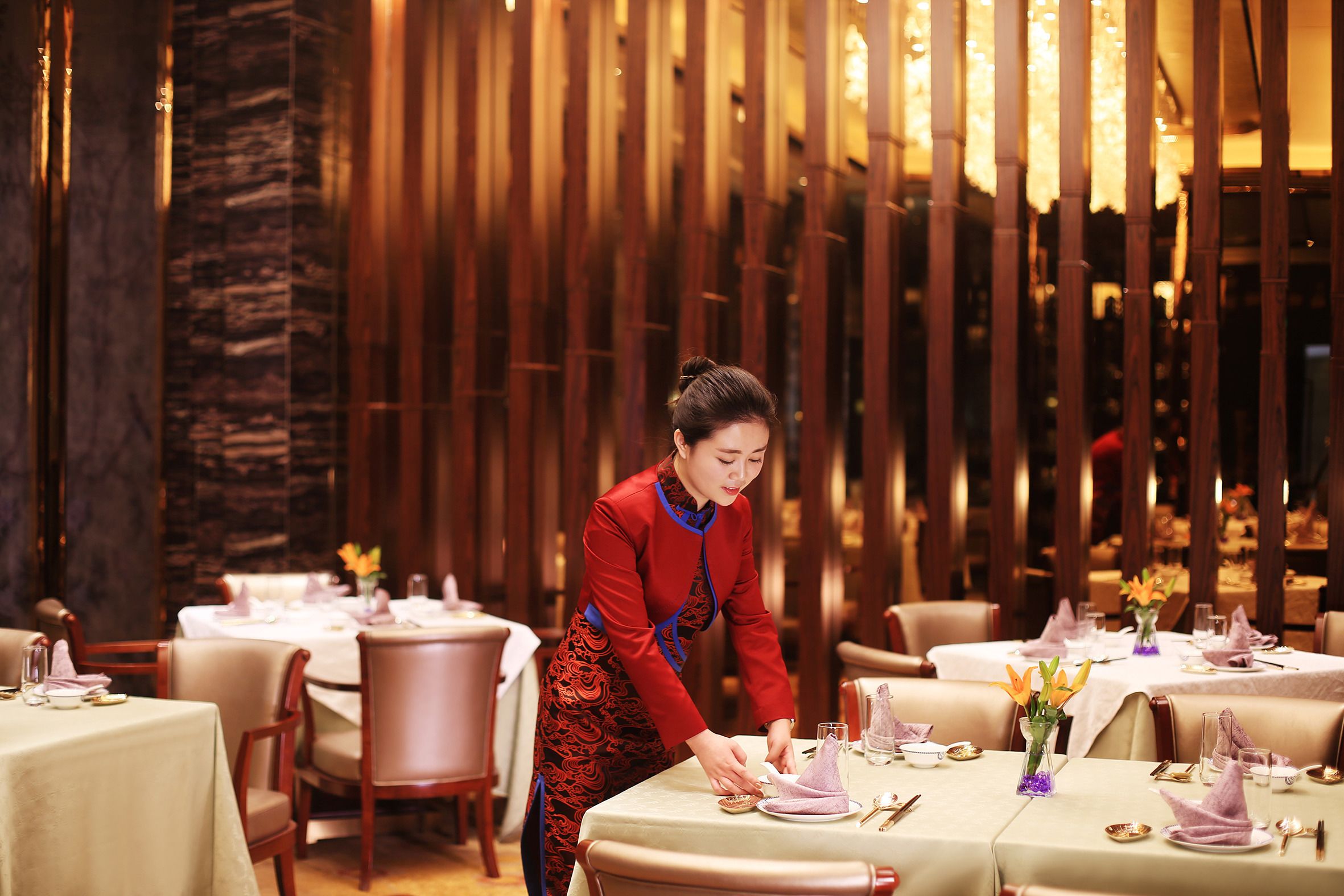 A restaurant with tables set for dining, a waitstaff attending to guests, and a warm interior ambiance.