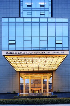 A modern building with a large illuminated entrance and a sign reading "Wyndham Grand Plaza Royale Huayu Chongqing".