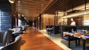 A modern restaurant with wooden floors, dark upholstered chairs, and a chef at the counter. - Wyndham Grand Plaza Royale Huayu Chongqing (Chongqing)
