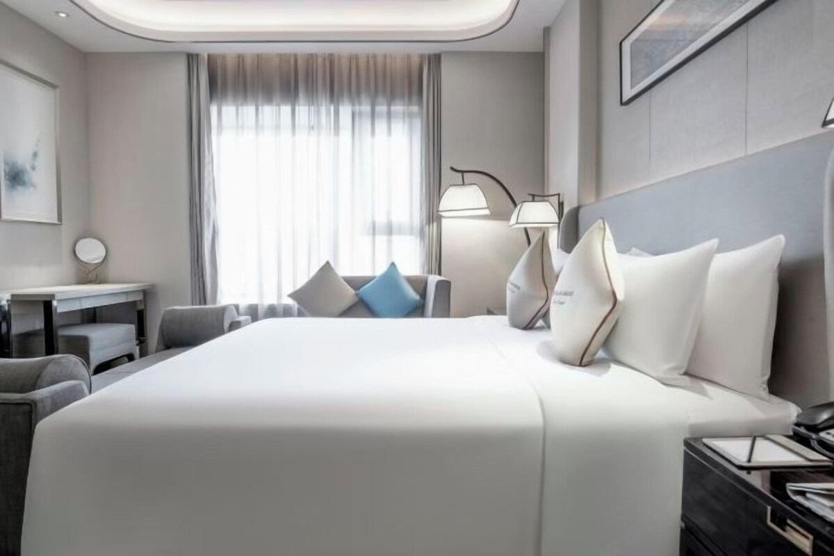 Une chambre d’hôtel avec un grand lit, une table de chevet, une lampe et une vue sur l’extérieur.