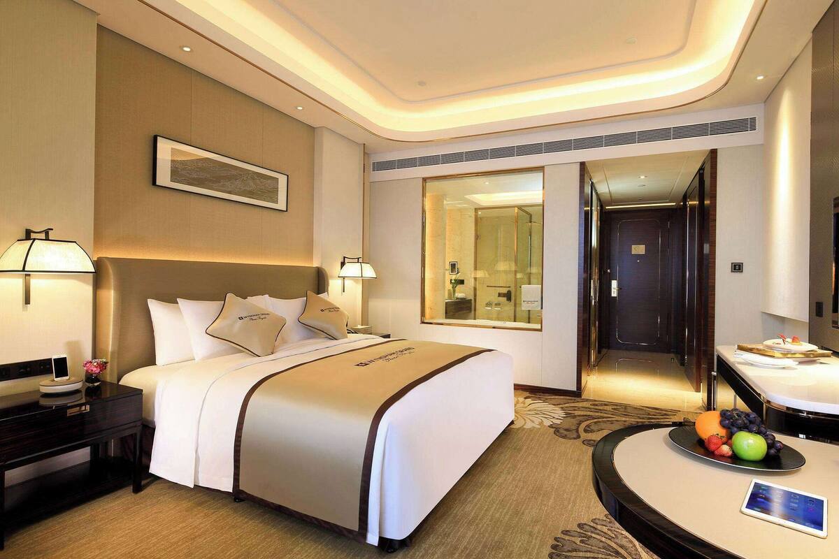 Une chambre d’hôtel avec un grand lit, des tables de chevet, un bureau et un panier de fruits.