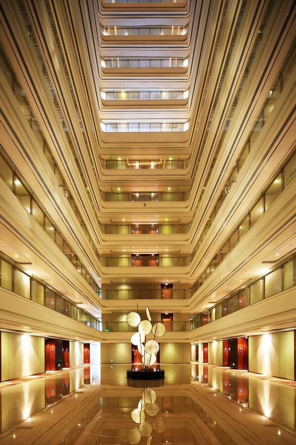 A multi-level hotel interior with a central atrium, reflective floors, and a modern design.