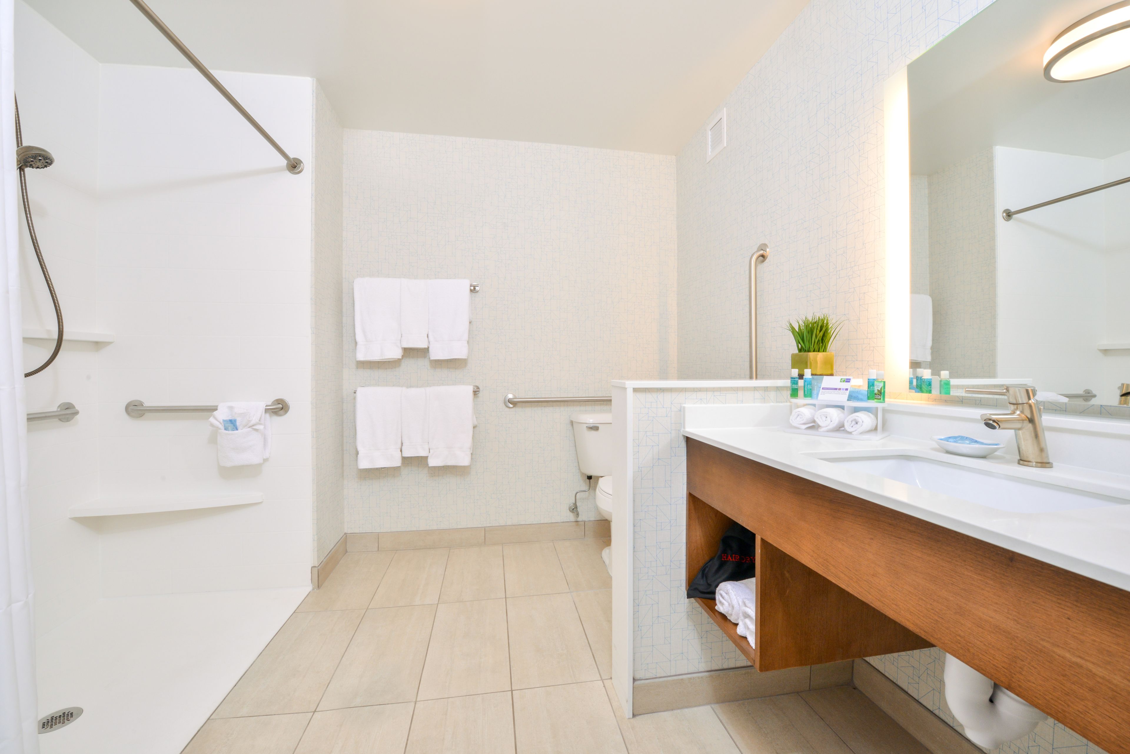 A modern bathroom with a shower, toilet, and sink. There are towels hanging on the wall, a mirror, and toiletries on the sink.