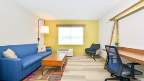 A room with a blue sofa, a wooden coffee table, a black office chair, a standing lamp, and a large window with a view. - Holiday Inn Express & Suites Salem by IHG (Salem)