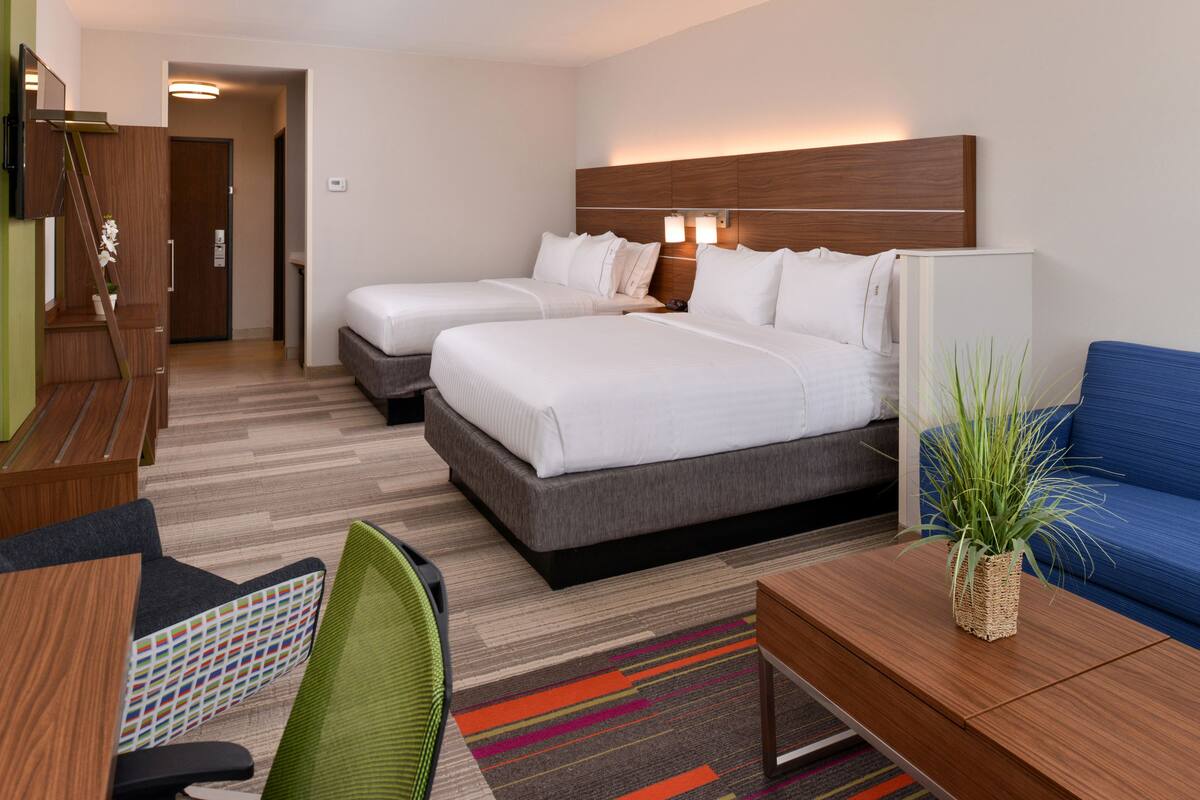 A hotel room with two beds, a desk, a chair, and a sofa.