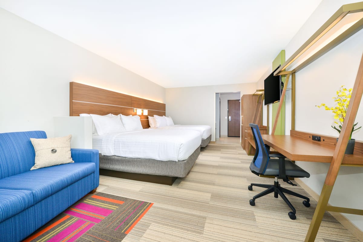 A hotel room with a bed, a desk, a chair, and a sofa.