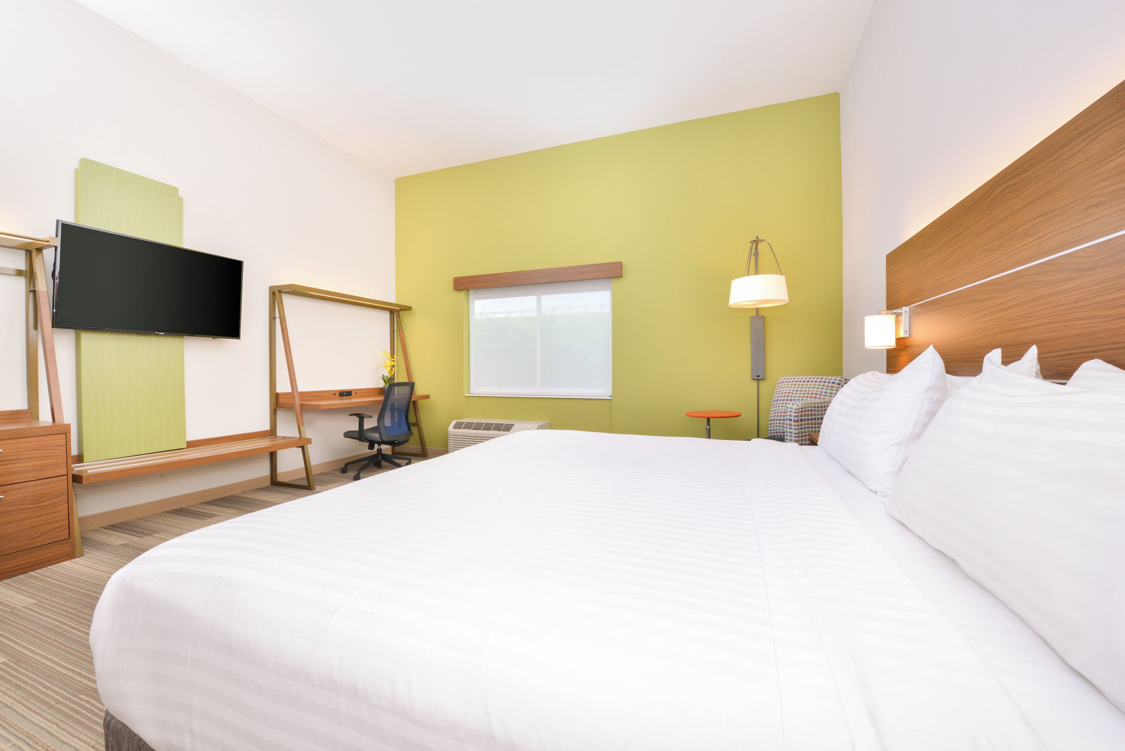 Une chambre d’hôtel avec un grand lit, un bureau, une chaise, une télévision, une fenêtre et une lampe.