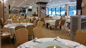 Un salón de banquetes con mesas redondas, sillas y un ventanal grande.
