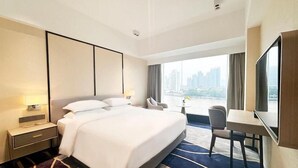 Habitación de hotel con una cama grande, un escritorio, una silla, un televisor y vistas a un paisaje urbano.