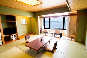 A room with tatami flooring, a wooden table, chairs, a television, and a view of the sea. - Naruto Grand Hotel (Naruto)