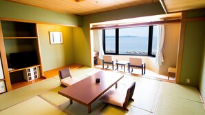 A room with tatami mats, a wooden table, chairs, a TV, and a view of the sea. - Naruto Grand Hotel (Naruto)