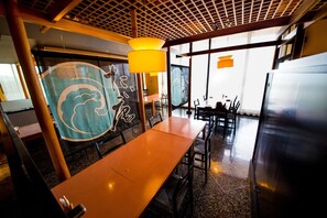 Interior de un restaurante con una mesa de madera, sillas, una lámpara colgante y un gran ventanal.