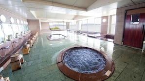 A large indoor pool area with multiple shower stations and a central hot tub. - Naruto Grand Hotel (Naruto)