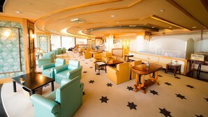 Un vestíbulo de hotel con techo curvo, zonas de estar con sofás y sillones, una zona de bar y un ventanal grande.