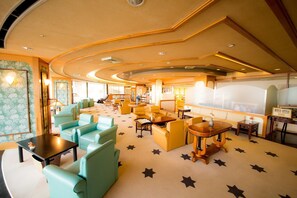 A spacious lounge area with multiple seating options including sofas and armchairs, a central coffee table, and a small bar area. - Naruto Grand Hotel (Naruto)