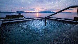 Un jacuzzi con vistas a una puesta de sol sobre el agua, un puente y montañas distantes.