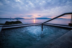 A hot tub with a view of a sunset over water, a bridge in the distance, and a railing. - Naruto Grand Hotel (Naruto)