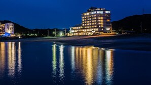 Un hotel de varios pisos con una piscina reflectante en primer plano, rodeado de colinas.